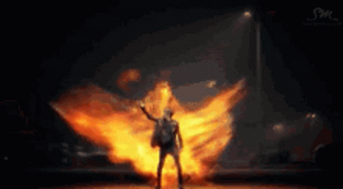 a man is standing in front of a huge explosion of fire .