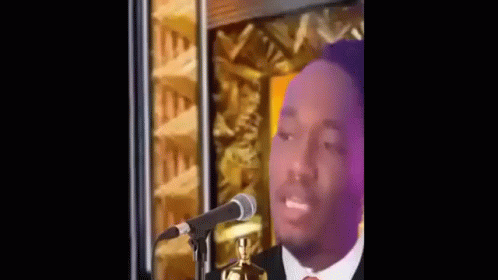 A Man Is Standing In Front Of A Microphone And Talking Into It . GIF