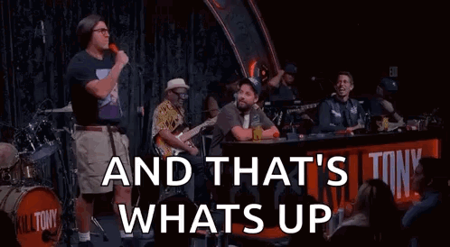 A Man Is Standing In Front Of A Microphone On A Stage With A Band Behind Him . GIF