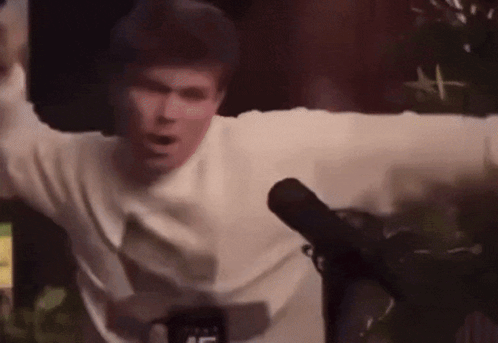 A Man Is Standing In Front Of A Microphone With His Arms Outstretched GIF