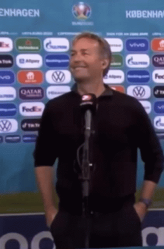 A Man Is Standing In Front Of A Microphone With His Hands In His Pockets . GIF