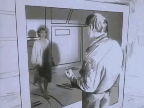 A Man Is Standing In Front Of A Mirror Looking At Himself In A Black And White Photo . GIF