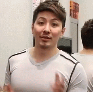 A Man Is Standing In Front Of A Mirror Wearing A White Shirt And Making A Funny Face . GIF