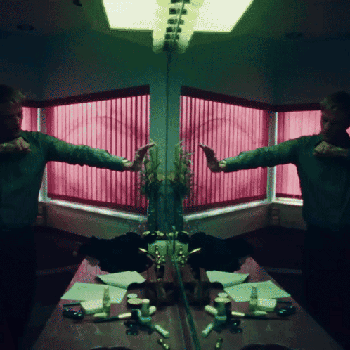 A Man Is Standing In Front Of A Mirror With A Pink Window Behind Him GIF