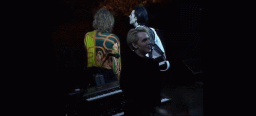a man is standing in front of a piano on a stage while a woman stands behind him .