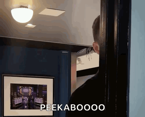 A Man Is Standing In Front Of A Picture That Says Peekaboooo On It GIF