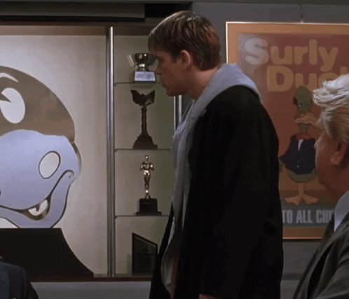 A Man Is Standing In Front Of A Poster That Says Surly Duck GIF
