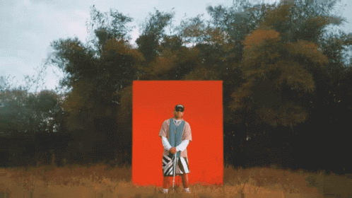 A Man Is Standing In Front Of A Red Box In A Field GIF