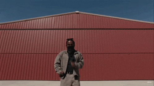 A Man Is Standing In Front Of A Red Building That Says Vevo On The Bottom Right GIF