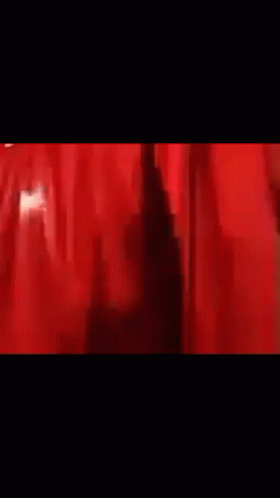 A Man Is Standing In Front Of A Red Curtain In A Dark Room . GIF