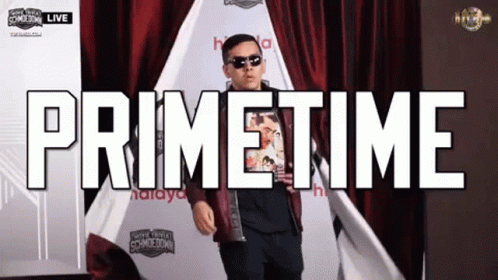 A Man Is Standing In Front Of A Red Curtain With The Words Primetime Written Above Him GIF