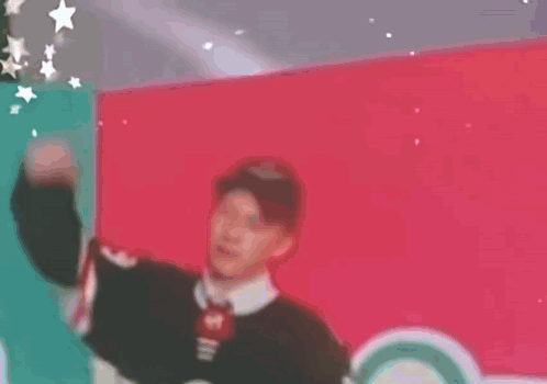 A Man Is Standing In Front Of A Red Wall And Making A Funny Face . GIF
