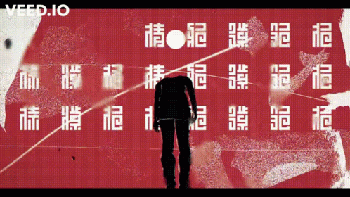 A Man Is Standing In Front Of A Red Wall With Chinese Characters And The Word Veed.io On The Bottom GIF