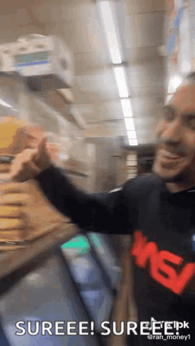 A Man Is Standing In Front Of A Refrigerator In A Store And Giving A Thumbs Up . GIF