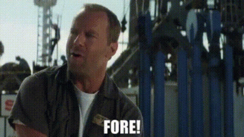 A Man Is Standing In Front Of A Roller Coaster Holding A Piece Of Paper And Saying Fore . GIF