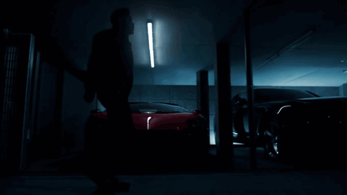 A Man Is Standing In Front Of A Row Of Cars In A Dark Garage GIF