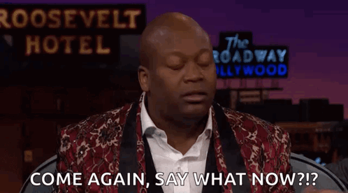 A Man Is Standing In Front Of A Sign That Says `` Come Again , Say What Now ? '' . GIF
