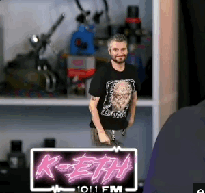 A Man Is Standing In Front Of A Sign That Says K-Eth On It GIF