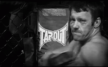 A Man Is Standing In Front Of A Sign That Says Tapout On It . GIF