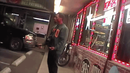 A Man Is Standing In Front Of A Store That Says Rockstar Energy Drink GIF