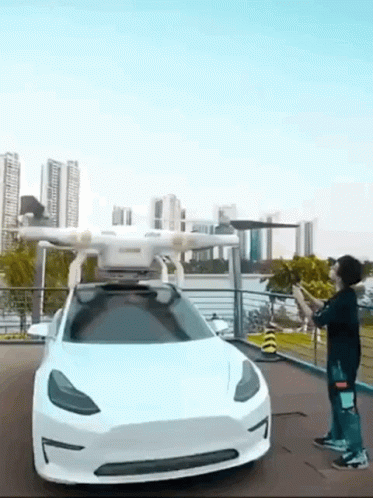 A Man Is Standing In Front Of A Tesla Model 3 With A Drone Attached To It . GIF