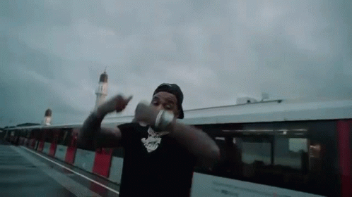 A Man Is Standing In Front Of A Train Holding A Bottle Of Water . GIF