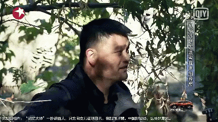 A Man Is Standing In Front Of A Tree With Chinese Writing On The Bottom Right GIF