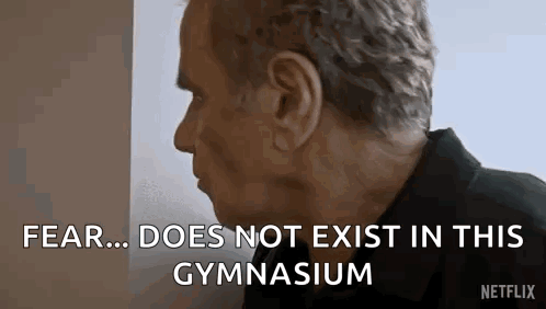 A Man Is Standing In Front Of A Wall And Talking About Fear Does Not Exist In This Gymnasium . GIF