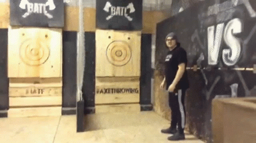 A Man Is Standing In Front Of A Wall That Says Axe Throwing On It GIF
