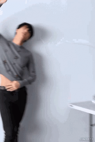 A Man Is Standing In Front Of A Wall With His Shirt Off And Holding His Stomach . GIF