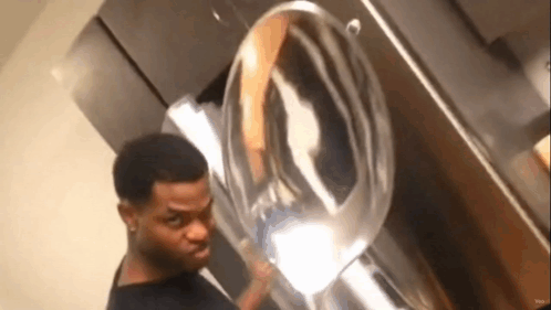 A Man Is Standing In Front Of A Washing Machine And Looking At The Reflection Of Himself In The Mirror . GIF