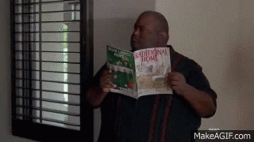A Man Is Standing In Front Of A Window Holding A Book Titled Traditional Home . GIF