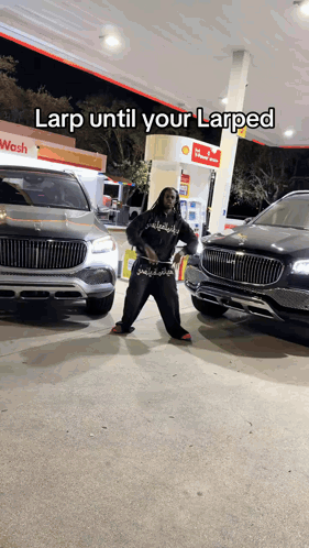A Man Is Standing In Front Of Two Cars At A Gas Station With A Caption That Says Larp Until Your Larped GIF
