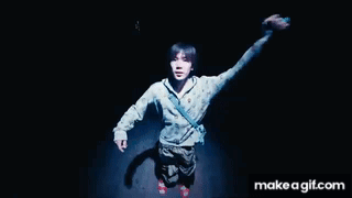 A Man Is Standing In The Dark With His Arms In The Air .. GIF