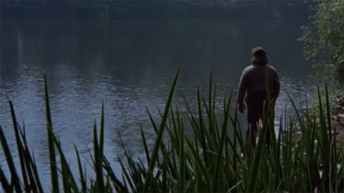 a man is standing in the grass near a lake