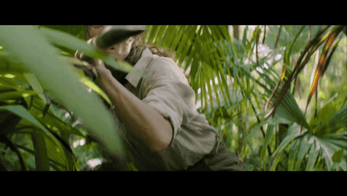 a man is standing in the jungle looking through a leaf