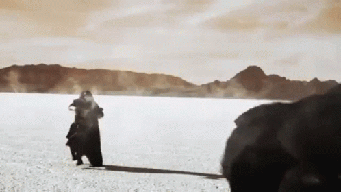 A Man Is Standing In The Middle Of A Desert Holding A Baby . GIF