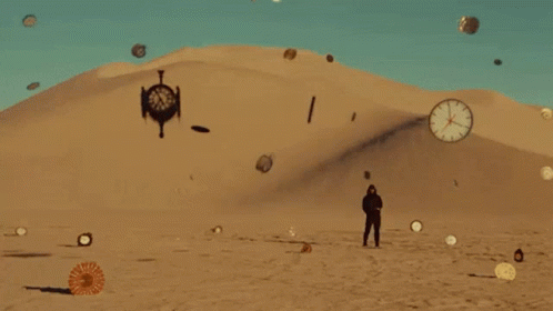 A Man Is Standing In The Middle Of A Desert With Clocks Flying Around Him . GIF