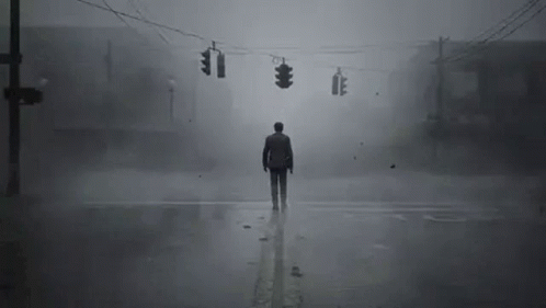 A Man Is Standing In The Middle Of A Foggy Street At An Intersection . GIF