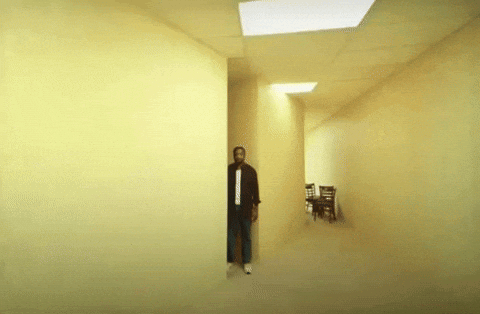 A Man Is Standing In The Middle Of A Hallway With A Light On The Ceiling GIF