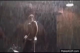 A Man Is Standing In The Rain With A Boxing Glove In His Hand . GIF