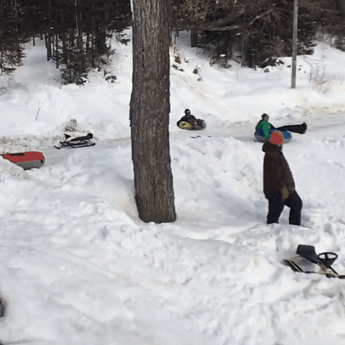A Man Is Standing In The Snow Near A Tree GIF
