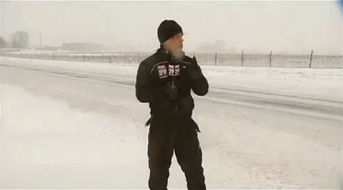 A Man Is Standing In The Snow With His Arms Outstretched In Front Of A Large Truck . GIF