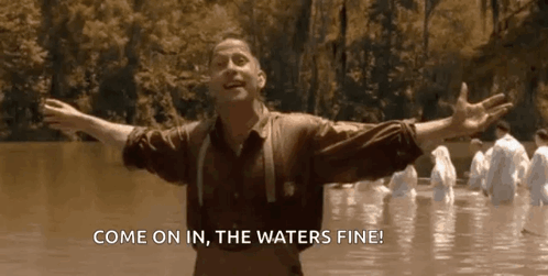 A Man Is Standing In The Water With His Arms Outstretched And A Group Of People Are Standing In The Water . GIF