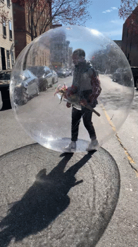 A Man Is Standing Inside Of A Clear Bubble On The Sidewalk GIF