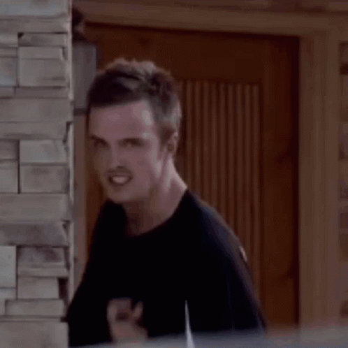 A Man Is Standing Next To A Brick Wall And Making A Funny Face With His Finger In His Mouth . GIF