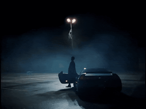 A Man Is Standing Next To A Car In A Dark Parking Lot GIF