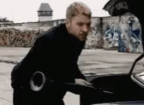 A Man Is Standing Next To A Car With The Hood Open . GIF