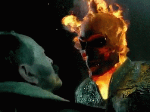 A Man Is Standing Next To A Ghost Rider With Flames Coming Out Of His Face . GIF