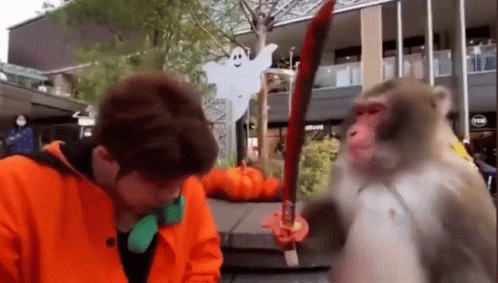 A Man Is Standing Next To A Monkey Holding A Sword In Front Of A Building . GIF